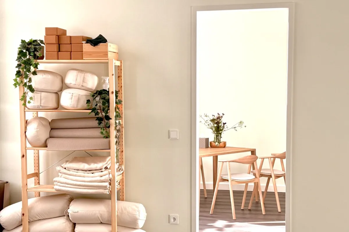 Yoga room at Kaiserufer Hamburg with a shelf full of cushions and mats, view into the next room